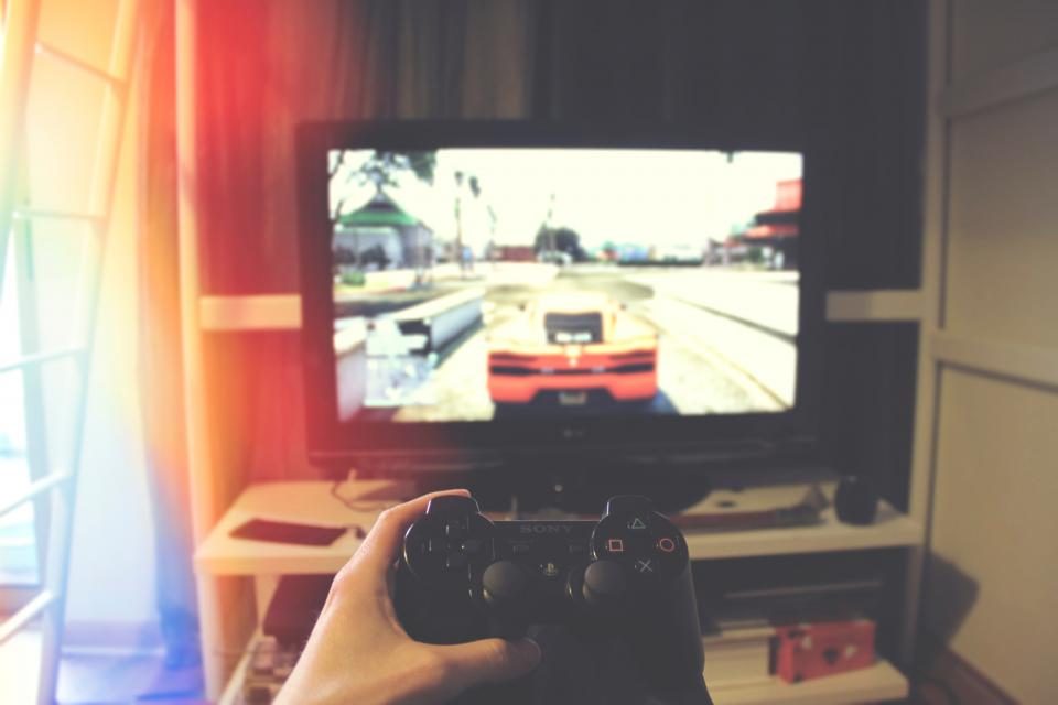 En hånd holder en PlayStation-controller foran et fjernsyn med et racerspil