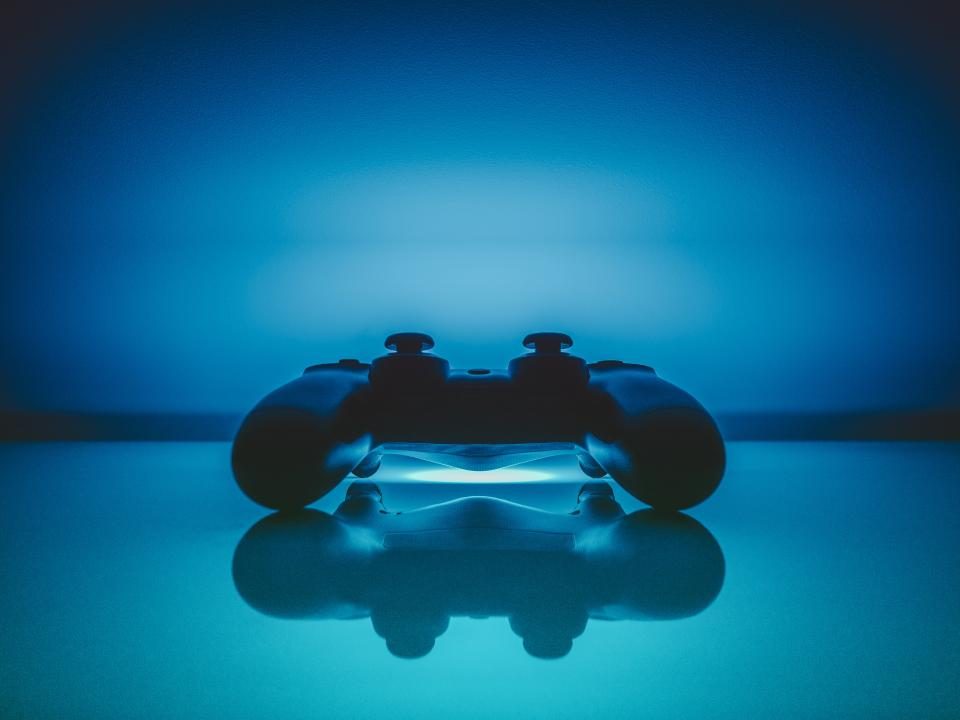 En PlayStation-controller i silhuet på et blankt bord i blåt lys