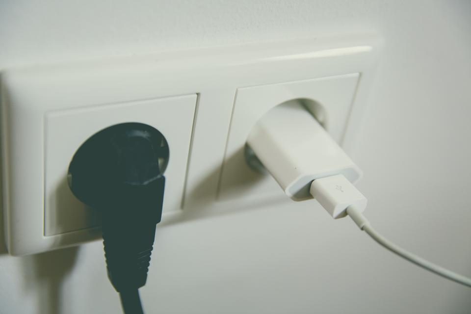 Et sort stik og en hvid USB-oplader sat i en dobbelt stikkontakt på en hvid væg